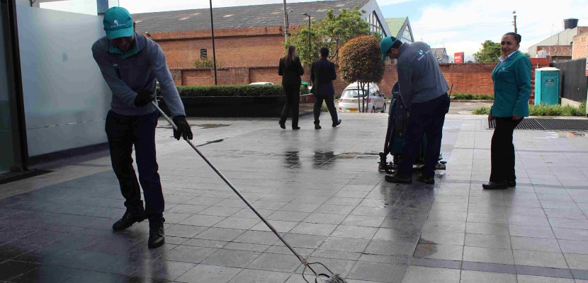 Trabajador realiza limpieza de fachada con trapero mientras es supervisado