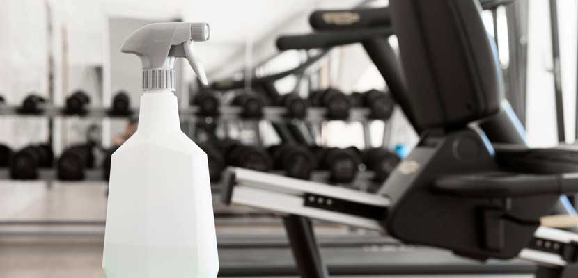 Plano cerrado de spray para limpiar sobre maquina de gimnasio mostrando la limpieza de instalaciones deportivas con Misión Servir
