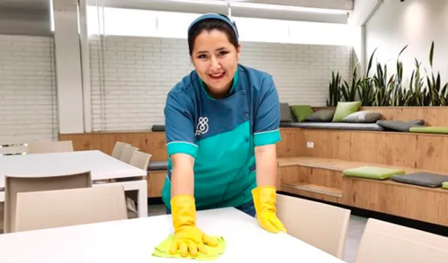 Mujer realizando limpieza en mesa mostrando los beneficios de contratar empresa de aseo para edificios corporativos